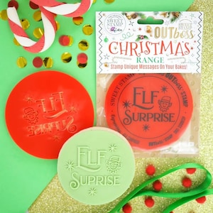 May include: Two red and green round cookie cutters with the text "Elf Surprise" and a small elf illustration. The cutters are packaged in a clear plastic bag with a white label that says "Outboss Christmas Range" and "Sweet Stamp".