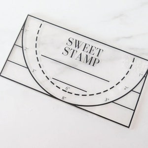 May include: A clear plastic stamping tool with a semi-circle guide and measurements in inches. The tool is labeled "SWEET STAMP".
