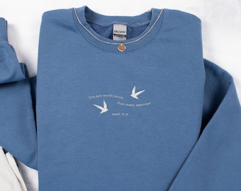 May include: A blue sweatshirt with the text "You are worth more than many sparrows Matt 10:31" embroidered on the front. The sweatshirt has a crew neck and long sleeves.
