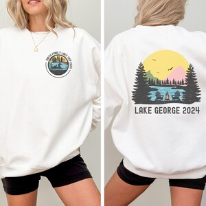 Puede incluir: Sudadera blanca con un gr&aacute;fico circular en la parte delantera que dice "Smith Family Lake Trip 2021" y un gr&aacute;fico en la parte trasera que dice "Lake George 2024" con una escena de lago y una puesta de sol.