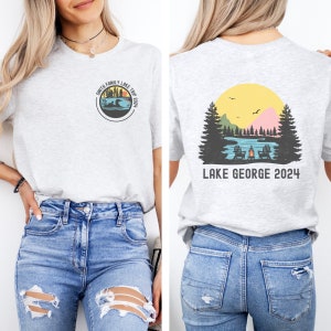 May include: A gray t-shirt with a circular design on the front that says "Smith Family Lake Trip 2024" and a graphic of a lake with a loon. The back of the shirt has a graphic of a lake scene with a campfire and the text "Lake George 2024".