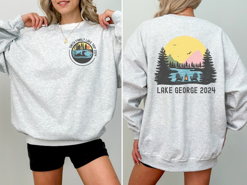 Puede incluir: Sudadera gris con un gr&aacute;fico de una escena de lago con &aacute;rboles, una fogata y dos sillas en la espalda. La parte delantera de la sudadera tiene un gr&aacute;fico circular con el texto "Smith Family Lake Trip 2024".