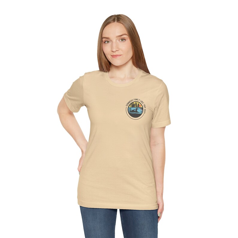 May include: A light beige t-shirt with a vintage-style graphic on the front. The graphic features a sunset scene with a lake, trees, and the text "Summers I like the best".