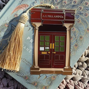 May include: A decorative bookmark featuring a burgundy door design with the text "A.Z. FELL AND Co." The bookmark has a gold tassel and is set against a book with peacock feather illustrations.