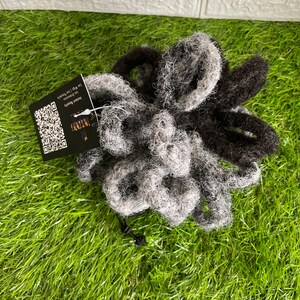 May include: A bundle of gray and black dreadlocks with a tag attached. The dreadlocks are arranged in a loose pile on a green surface. The tag has a QR code and text that reads "Instant Beauty".