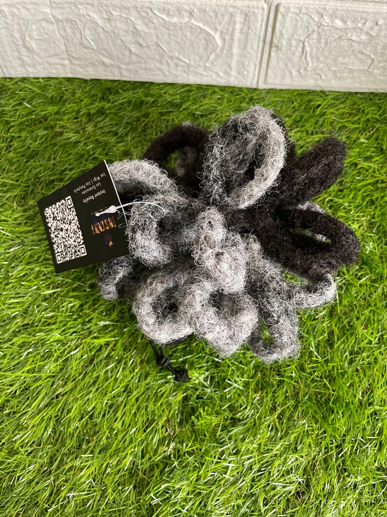 May include: A bundle of gray and black dreadlocks with a tag attached. The dreadlocks are arranged in a loose pile on a green surface. The tag has a QR code and text that reads "Instant Beauty".