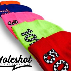 May include: Five colorful beanies with checkered numbers on them. The beanies are stacked on top of each other. The numbers are 1, 3, 10, 5, and 11. The beanies are in the colors orange, blue, pink, green, and red. The text "Holeshot Family Racing Gear" is at the bottom of the image.