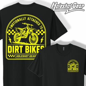 May include: A black t-shirt featuring a large yellow graphic on the back and a smaller matching version on the front left chest. The design shows a dirt bike, checkered patterns, lightning bolts, and the text "EMOTIONALLY ATTACHED TO DIRT BIKES" and "HOLESHOT GEAR".