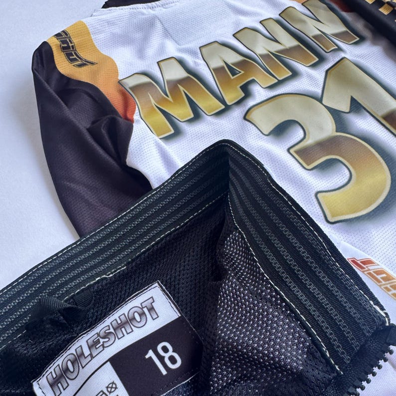 May include: Black and white motocross jersey with a black and white mesh panel. The jersey has a white label with the text "HOLESHOT" and the number "18" printed on it.