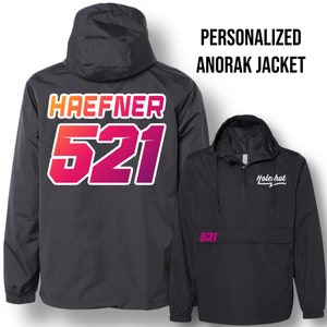 Peut inclure: Veste anorak noire avec un nom et un numéro personnalisés au dos. Le nom est "HAEFNER" et le numéro est "521". La veste a une fermeture éclair et une poche sur le devant. La poche avant porte le texte "Hole hat".