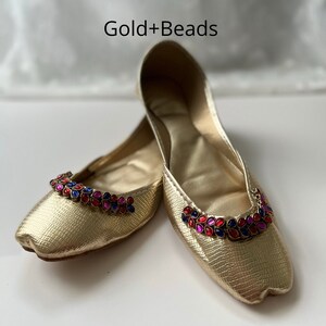May include: A pair of gold flats with a beaded embellishment. The beads are in shades of red, pink, blue, and gold.