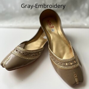May include: A pair of gray leather flats with gold embroidery. The shoes have a pointed toe and a flat heel.