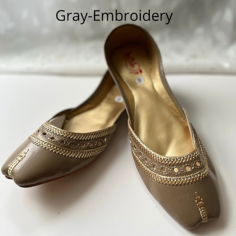 May include: A pair of gray leather flats with gold embroidery. The shoes have a pointed toe and a flat heel.