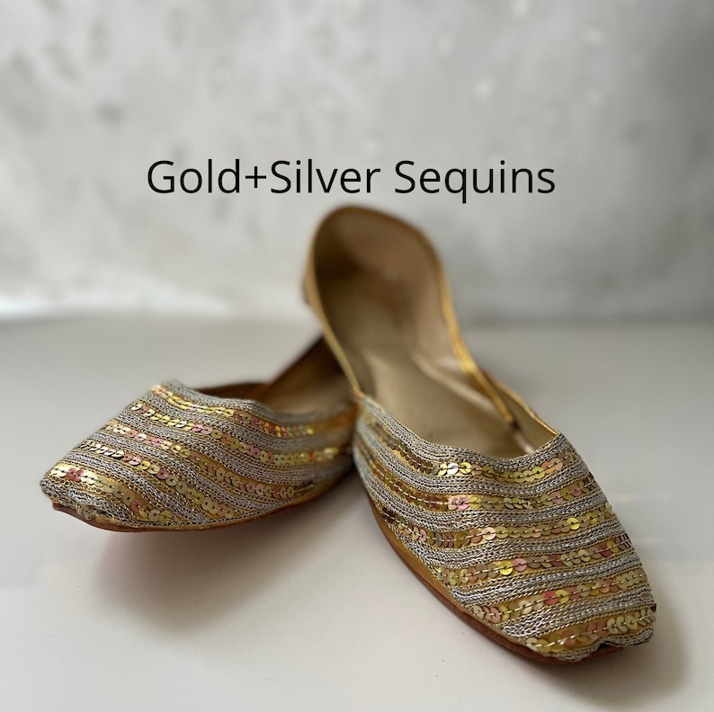 May include: A pair of gold and silver sequined flat shoes. The shoes have a pointed toe and are made of a soft, flexible material.