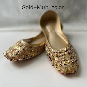 May include: A pair of gold flat shoes with colorful embroidery and sequins. The shoes have a pointed toe and a low heel.