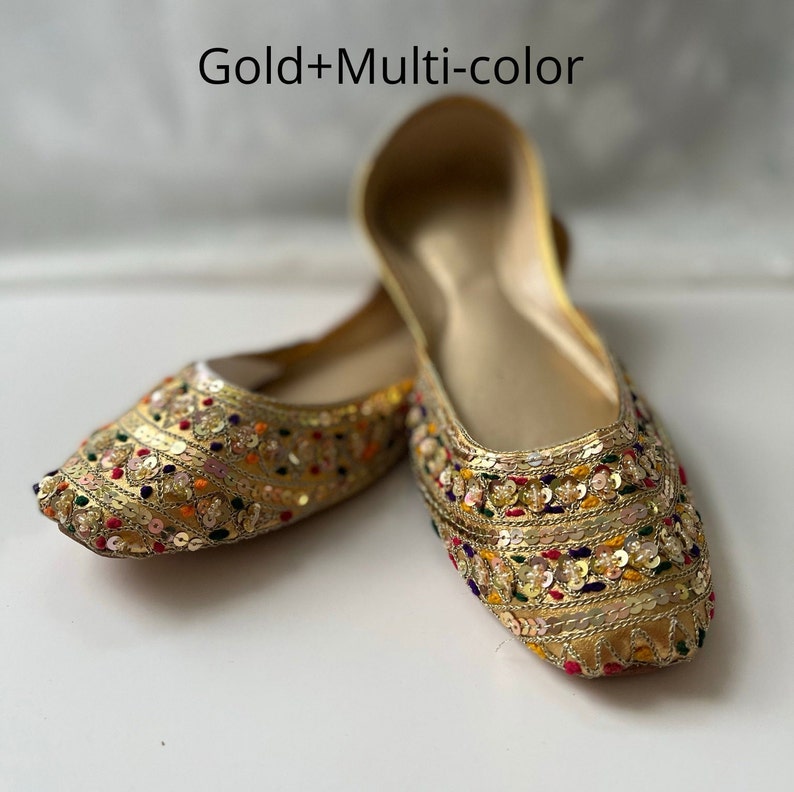 May include: A pair of gold flat shoes with colorful embroidery and sequins. The shoes have a pointed toe and a low heel.