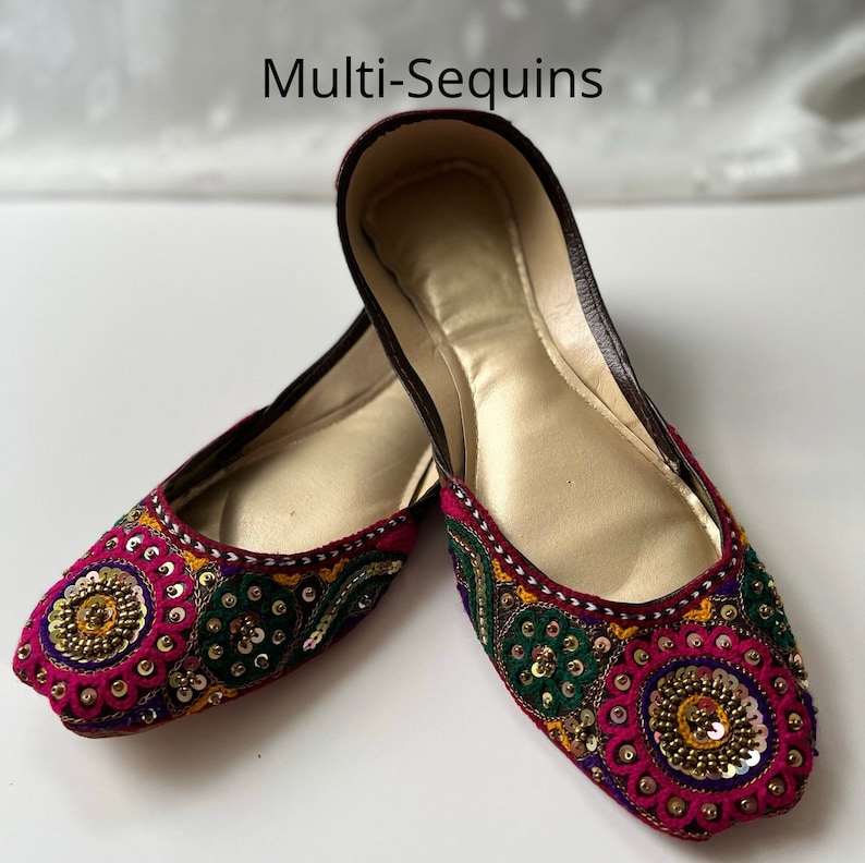 May include: A pair of flat, burgundy shoes with gold, green, and pink embroidery and sequins. The shoes have a pointed toe and a flat sole.