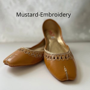 May include: A pair of mustard-colored leather flats with gold embroidery. The flats have a pointed toe and a delicate, intricate design.