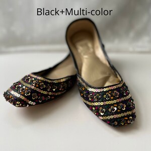 May include: A pair of black flat shoes with colorful embroidered floral patterns and sequins. The shoes have a gold lining.