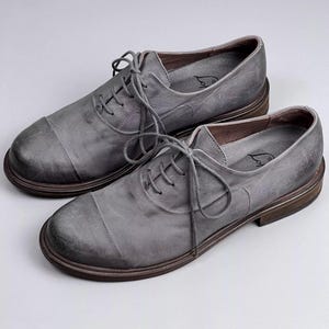May include: A pair of gray leather lace-up shoes with a distressed finish. The shoes have a rounded toe and a thick sole.