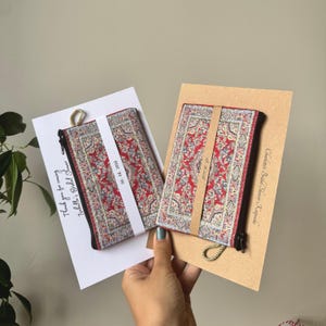 May include: Two small, rectangular pouches with a red and floral pattern, resembling miniature rugs, are displayed with cards. One card reads "Thank you for coming Isabella's Bridal Shower". The other card reads "Charlotte's Bridal Shower Keepsake".