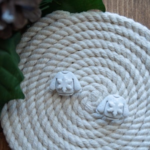 Könnte beinhalten: Zwei weiße Keramik-Weihnachtspullover-Ornamente mit Schneeflocken-Design auf einem weißen Seil-Hintergrund.