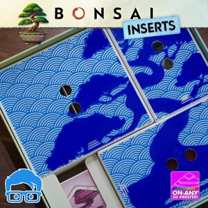 Op de afbeelding: Een doos met blauwe en witte golfpatroon inzetstukken, met een blauw boomontwerp. Het woord "BONSAI" staat bovenaan, met "INSERTS" op een label. De afbeelding bevat ook een kleine bonsai boom illustratie en een afbeelding met de tekst "MULTICOLOR ON ANY 3D PRINTER!"
