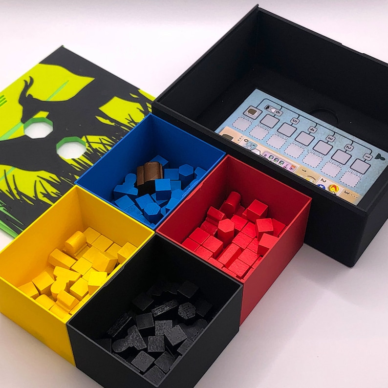 May include: A black box with four compartments filled with colorful wooden blocks. The compartments are labeled with numbers 1 through 4. The box is open and the lid is on the right side of the image. The lid has a blue and white card with text and symbols.