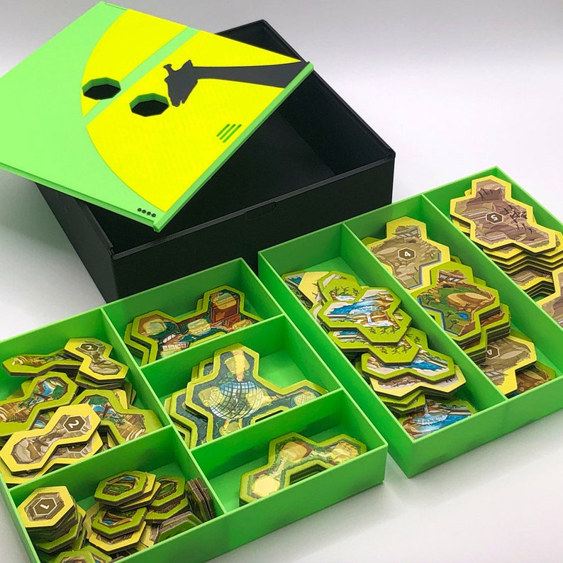 May include: A green storage box with a yellow lid featuring a silhouette of a giraffe. The box is open and contains multiple compartments filled with colorful game pieces.