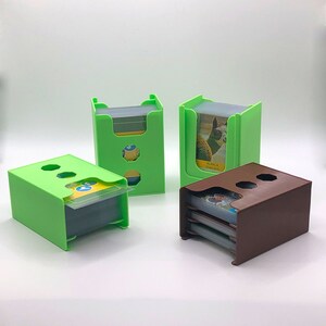 May include: Three green and brown card holders with slots for holding multiple decks of cards. The card holders are made of plastic and have a simple design.