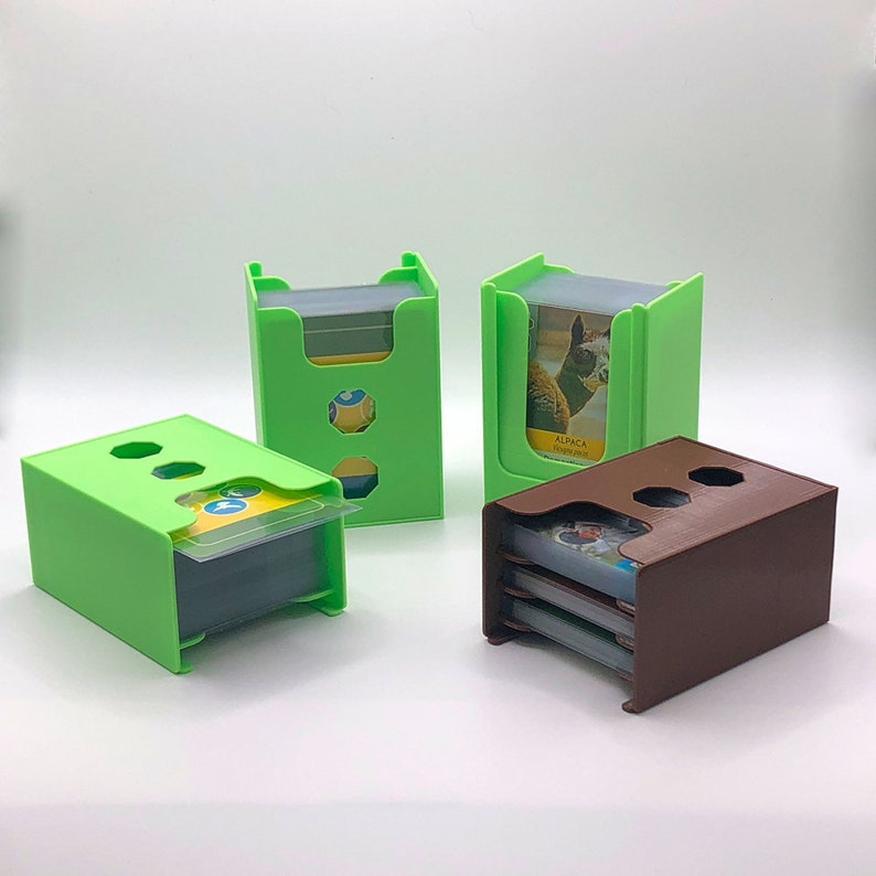 May include: Three green and brown card holders with slots for holding multiple decks of cards. The card holders are made of plastic and have a simple design.