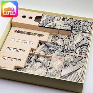 Può includere: Una scatola beige con un inserto beige che contiene un gioco con illustrazioni di animali in bianco e nero. La scatola è aperta e le pedine del gioco sono visibili. Le pedine del gioco sono in legno e hanno un design in bianco e nero.