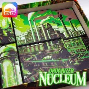 May include: A board game organizer box with a green and brown industrial factory design. The word "ORGANIZER" is above the word "NUCLEUM" in a glowing green font. The box contains several game tiles with the same factory illustration.