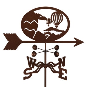 May include: A brown metal wind vane with a silhouette of hot air balloons and mountains. The wind vane has a compass rose with the letters W, S, E, and N.