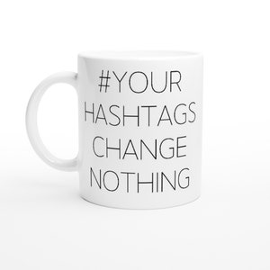 May include: White ceramic mug with black text that reads "#YOUR HASHTAGS CHANGE NOTHING".