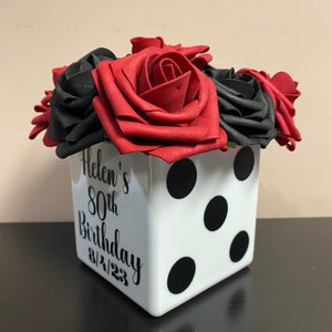May include: A white ceramic cube with black polka dots and the text "Helen's 80th Birthday 8/21/23" is filled with red and black foam roses.