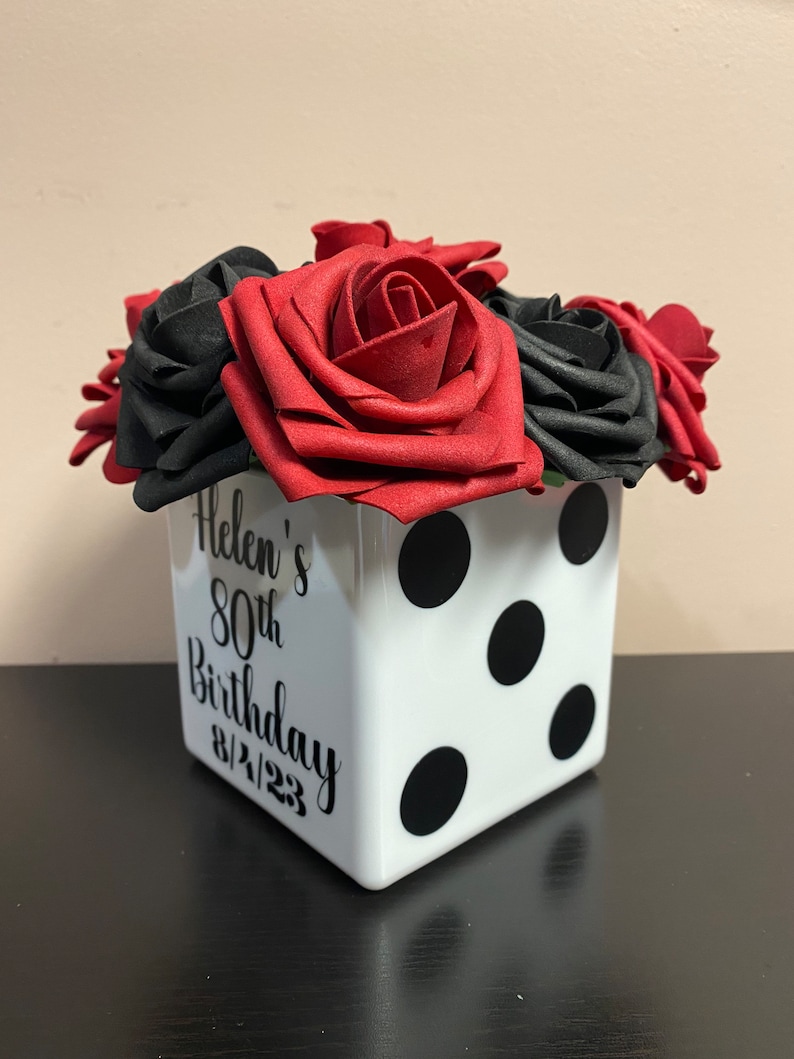 May include: A white ceramic cube with black polka dots and the text "Helen's 80th Birthday 8/21/23" is filled with red and black foam roses.