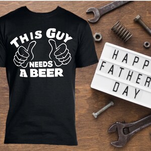 May include: Black t-shirt with white text that reads "This Guy Needs A Beer" with two thumbs up symbols. A white light-up sign reads "Happy Fathers Day".