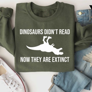 May include: A green sweatshirt with the text "Dinosaurs didn't read now they are extinct" and a white silhouette of a dinosaur.