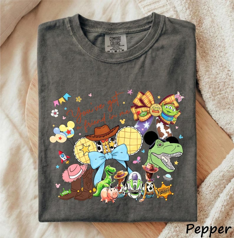 A gray t-shirt with a colorful graphic design featuring various characters from the Toy Story franchise, including Woody, Buzz Lightyear, and other beloved characters.