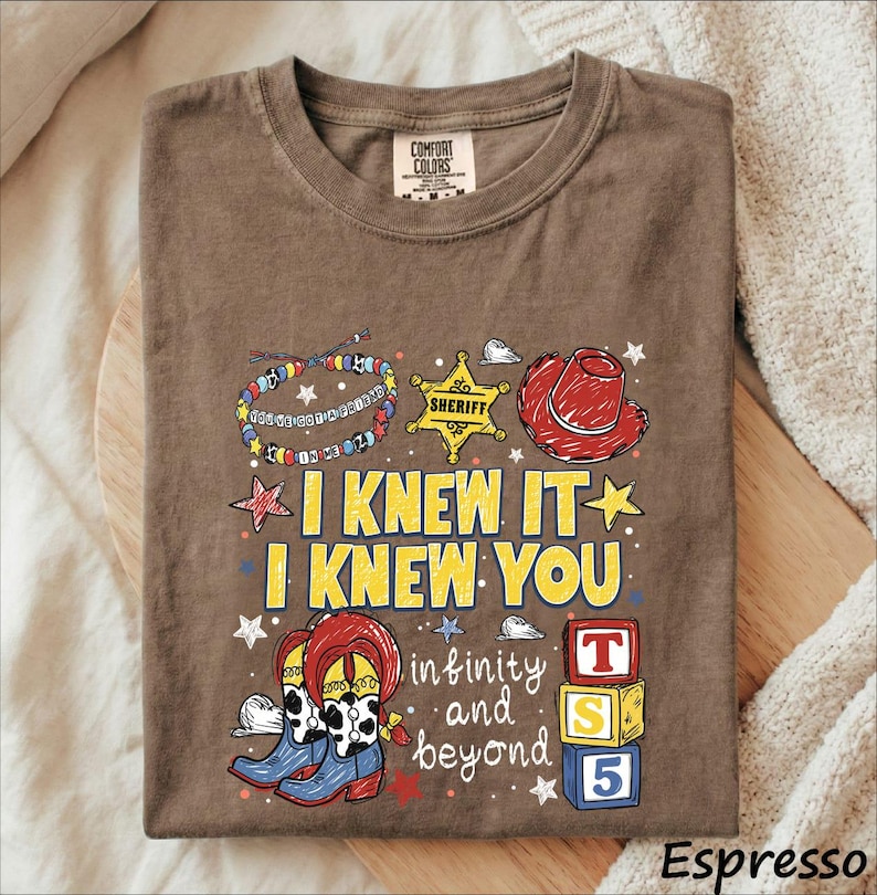 A t-shirt with a cartoon-style design featuring a cowboy hat, a sheriff's badge, and various other cartoon-style elements. The text on the t-shirt reads "I KNEW IT I KNEW YOU in infinity and beyond" and includes a reference to the character Toy Story.