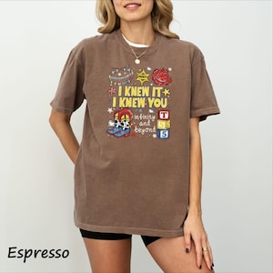 A woman wearing a brown t-shirt with a colorful graphic design and text printed on it.