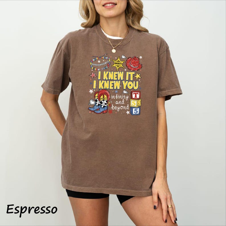 A woman wearing a brown t-shirt with a colorful graphic design and text printed on it.