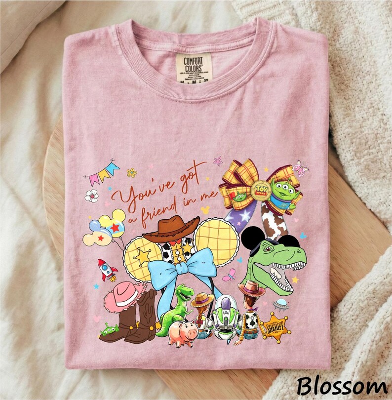 A pink t-shirt with a cartoon-style illustration of various characters from the Toy Story franchise, including Woody, Buzz Lightyear, and other beloved characters.