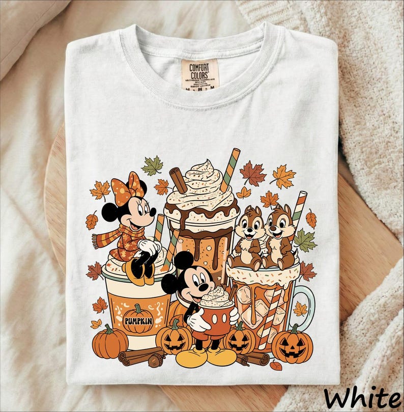 May include: A white t-shirt featuring a graphic print of Minnie Mouse, Mickey Mouse, and Chip 'n Dale with autumn-themed drinks. The design includes falling leaves, pumpkins, and cinnamon sticks. The shirt has a Comfort Colors brand neck label.