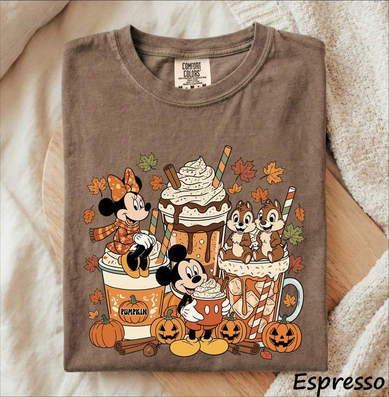May include: A brown t-shirt featuring a graphic of Minnie Mouse, Mickey Mouse, and Chip 'n Dale with pumpkin spice lattes and jack-o'-lanterns. The design includes autumn leaves, whipped cream, and the text Comfort Colors on the inner neck label.