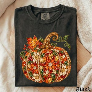 May include: A charcoal gray crew neck t-shirt featuring a large graphic of a pumpkin composed of colorful, faceted, jewel-toned floral patterns in shades of orange, yellow, red, and green, with a Comfort Colors brand label at the inner neckline.