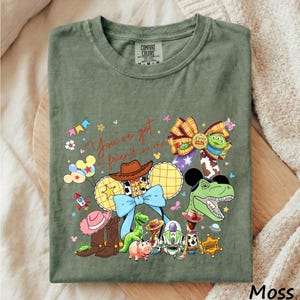 A green t-shirt with a colorful graphic design featuring characters from the Toy Story movie, including Woody, Buzz Lightyear, and other beloved characters.