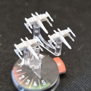 Könnte beinhalten: Drei weiße X-Wing-Sternenjäger auf einem durchsichtigen Plastikständer mit einer schwarz-weißen nummerierten Basis.