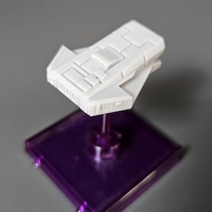 May include: A white plastic spaceship model on a purple display stand. The spaceship has a rectangular shape with a pointed nose and a flat bottom.
